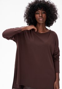 Bruine blouse met lange mouwen en een ontspannen pasvorm, met een ronde halslijn en zijsplitten, gemaakt van gladde, zachte stof.