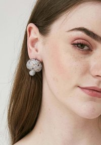 Runda, mångfacetterade örhängen med en silverfärgad bas; täckta av glittrande klara och färgade rhinestones, med en bubbelaktig design.