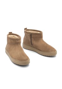 Paar beigefarbene Wildleder-Stiefeletten mit seitlichen Reißverschlüssen, beigen Gummisohlen und weichem Innenfutter vor weißem Hintergrund.