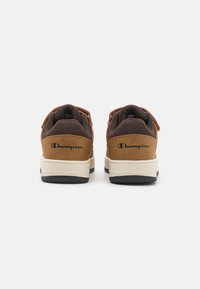 Zapatillas marrones y beige con un upper de tela texturizada, que cuentan con un logo en el talón, cierre de cordones y una entresuela blanca en contraste con la suela negra.