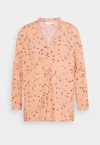 Světle broskvové tričko s dlouhým rukávem, výstřihem do V a rozptýlenými abstractními vzory v oranžové, černé a bílé barvě. Měkká tkanina s uvolněným střihem.