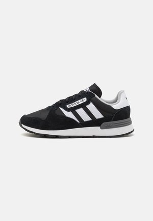 Baskets Adidas noir et blanc avec dessus en mesh et en daim, trois bandes blanches sur le côté et semelle rembourrée, vues de l'extérieur.