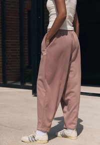 Roze joggingbroek van zachte stof met zijzakken, losse pasvorm, elastische tailleband en het woord "self." geborduurd nabij de zak.