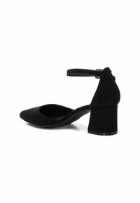 Zapato de tacón negro de ante con punta afilada, tira en el tobillo y tacón cuadrado. Textura suave y diseño minimalista sin herrajes visibles.