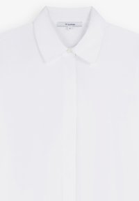 Camicia bianca con bottoni in cotone, caratterizzata da un colletto classico, chiusura con un singolo bottone e una finitura pulita e testurizzata. Etichetta del marchio visibile.
