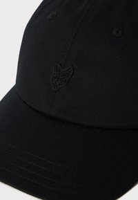 Casquette de baseball noire avec un petit logo de papillon brodé sur le panneau avant, montrant la texture du tissu et les détails de couture.