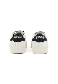 Sneakers bianchi con superficie testurizzata, dotati di dettagli neri sul tallone e di marchio. Suola piatta con un design semplice e minimalista.