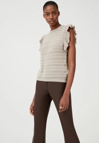 Top in maglia beige chiaro con maniche a volant e righe orizzontali, abbinato a pantaloni marroni aderenti. Texture liscia e design semplice.