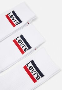 Hvide sokker med ribbet tekstur, der har "Levi's" logoet i sort, rød og marineblå på et farvet bånd nær toppen.
