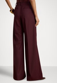 Platus kirpimo bordo spalvos kelnės iš lygios medžiagos. Turi diržo juosmenį ir galines kišenes su tvarkingu, pritaikytu apdailu.