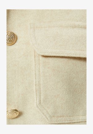 Beżowa kurtka z wełny z dodatkiem, z diamentowym złotym guzikiem i kieszenią na piersi o gładkiej, teksturowanej powierzchni.