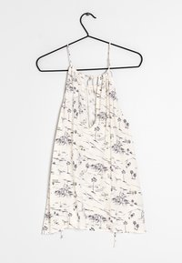 Krémový bezramínkový top s volným střihem, který má monochromatický potisk palmy a krajiny. Nastavitelná šňůrková uzávěrka na zadní straně.