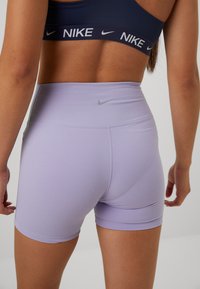 Lilat verkkarit, jotka on valmistettu joustavasta kankaasta, korkean vyötärön omaava malli ja takana pieni hopeinen Nike-logo.