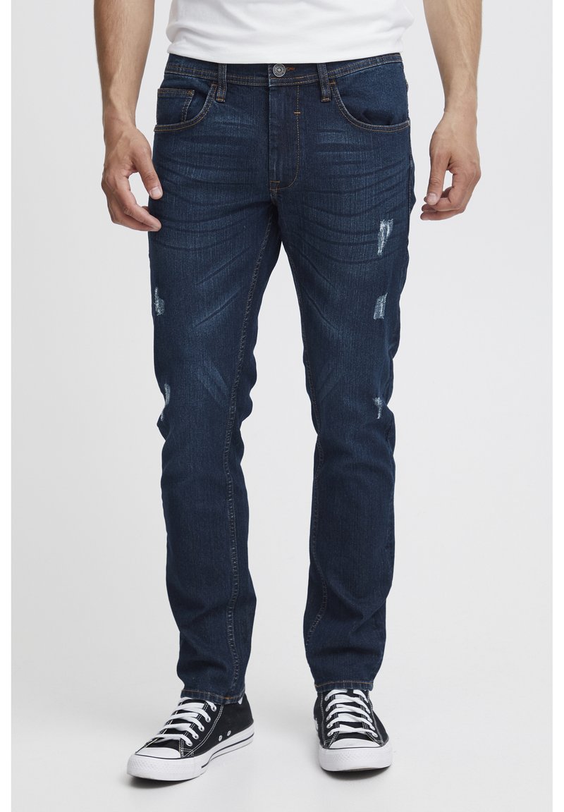 Tmavomodré denimové džínsy so slim fit strihom, s vybledlými detailmi a jemným prechodom farieb. Skombinované s čierno-bielymi plátennými teniskami.