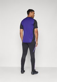 Completo sportivo composto da una maglietta a maniche corte viola e nera e leggings neri aderenti con accenti viola e un design testurizzato.