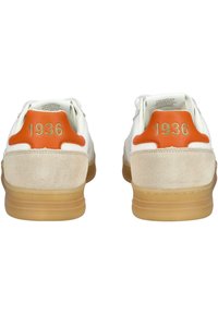Pár bílých tenisek s béžovými semišovými detaily, oranžovými patními taby a číslem "1936" vyraženým zlatem na každém patním tabu.