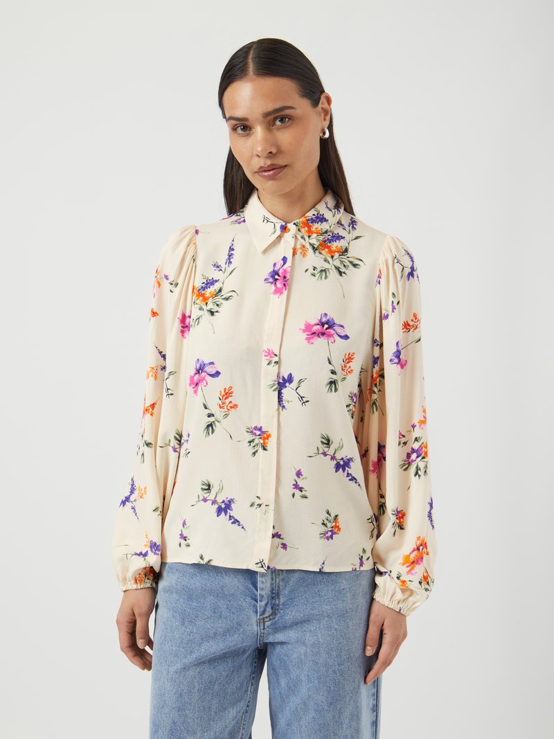 Blomstrete langermet bluse i kremfarge, med lilla, oransje og rosa blomster. Har krage med knapper og elastiske mansjetter.
