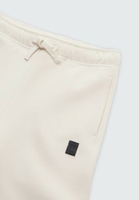 Crèmekleurige joggers met een elastische tailleband, trekkoorddetails, zijzakken en een klein zwart logopatch op het been.
