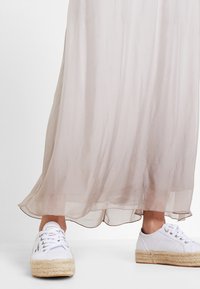 Vloeiende, lichtbeige jurk met een doorschijnende structuur, gecombineerd met witte platform sneakers met jute accenten en vetersluiting.