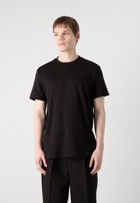 Juodas trumpas rankovės marškinėliai iš medvilnės su apvaliu kaklu; turi įspaustą 'Calvin Klein' logotipą kairėje krūtinės pusėje.
