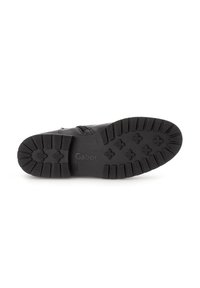 Suola di stivale nera con un design testurizzato, caratterizzata da un motivo di croci rialzate e scanalature per una maggiore aderenza. Marchio visibile sul lato.