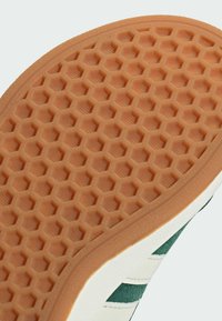 Potplat cipele s teksturiranim uzorkom saća, izrađen od gumene boje gume i off-white rubom s zelenim naglascima.