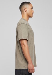 Camiseta de cuello redondo en verde oliva, fabricada en un tejido suave y texturizado, con mangas cortas y bajo recto, mostrada de lado.