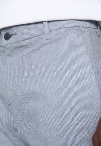 Jasnoniebieskie spodnie w wzorki z subtelnym kropeczkowym wzorem, płaskim przodem i pojedynczym zapięciem na guzik w pasie.