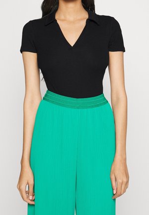 Czarny prążkowany body z dekoltem w kształcie V i kołnierzykiem, zestawione z zielonymi spodniami szerokimi w kant, posiadającymi teksturowany, pleciony pas.