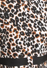 Leopardmønstret kjole med sorte og brune pletter på en hvid baggrund samt et sort bånd med teksten "Calvin Klein" ved taljen.