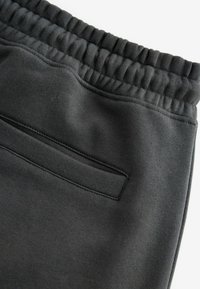 Schwarze Jogginghose mit einem elastischen Bund, versehen mit einer einzelnen Gesäßtasche und einer glatten Stoffoberfläche, entworfen für Komfort und Bewegungsfreiheit.