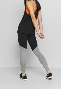 Czarno-szare legginsy sportowe z designem w kolorowe bloki, wykonane z elastycznego materiału. Uzupełnione luźną czarną bluzką na ramiączkach.