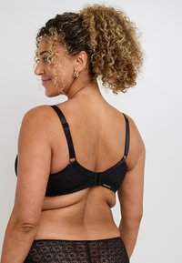 Soutien-gorge en dentelle noire avec bretelles réglables et fermeture à crochets. Doté d'un motif floral texturé. La vue de dos met en valeur les détails du cou et des épaules.