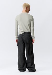 Ανοιχτό γκρι μακρυμάνικο πουκάμισο συνδυασμένο με υπερμεγέθη μαύρο τζιν παντελόνι που διαθέτει διπλές πίσω τσέπες και πλαϊνή τσέπη καρό.