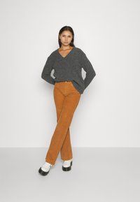 Gray v-neck sweater, loose fit; orange corduroy flared pants; white shoes with black soles; solid colors, textured materials.