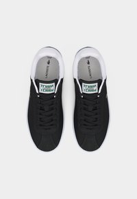 Ζευγάρι μαύρα αθλητικά παπούτσια τένις Lacoste με λευκές σόλες, λευκή επένδυση και πράσινο λογότυπο στη γλώσσα, απεικονιζόμενα από ψηλά σε λευκό φόντο.