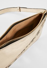 Borsa metallica dorata con chiusura a zip, foderata in nero e texture liscia. Presenta un design sottile, adatta per piccoli oggetti.