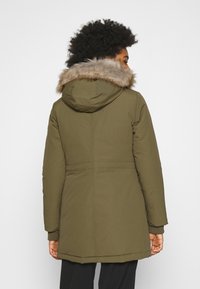 Olivgrön vadderad parkas med huva foder av fuskpäls, ribbade ärmslut och en lätt midja, som har en slät yta och dold dragkedja.