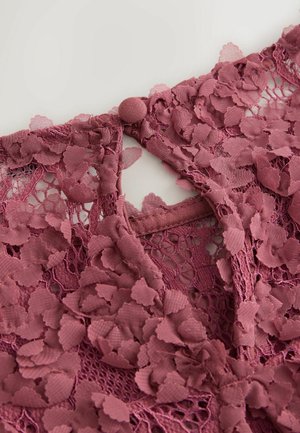 Růžově zbarvená krajková látka s květinovým vzorem, která má zapínání na knoflík na zadní straně a složitou texturu.