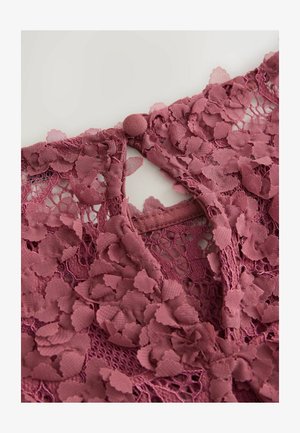 Vaaleanpunainen pitsikangas, jossa on kukkakuosi, napitus selkäpuolella ja monimutkainen tekstuuri.