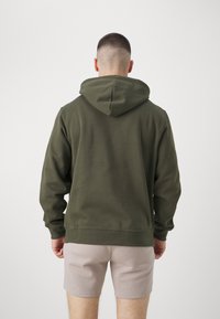 Felpa con cappuccio verde oliva, dal fit rilassato, maniche lunghe e polsini a costine, abbinata a pantaloni corti di un beige chiaro. Tessuto con una trama liscia.