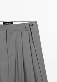 Šedé kalhoty na míru s předními záhyby, knoflíkem v pase a bočními kapsami. Hladká textilie s jednoduchým, klasickým designem.
