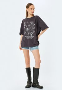 T-shirt oversized gris foncé avec un motif graphique cosmique blanc, associé à un short en denim bleu clair et des bottes noires jusqu'aux genoux.