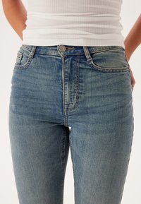 Hooggewaisted blauwe denim jeans met een vervaagde afwerking, subtiele wassing, gestikte accenten en een knoopsluiting bij de tailleband.
