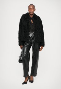 Μαύρο φ fuzzy μπουφάν, διαφανής μαύρη μπλούζα, μαύρο δερμάτινο παντελόνι με αντίθεση ραφών και μυτερές μαύρες γόβες. Μικρή τσάντα αξεσουάρ.