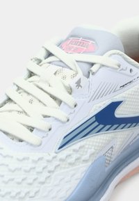 Λευκό αθλητικό παπούτσι με ανοιχτό μπλε λεπτομέρειες, πλέγμα υφής και μοτίβο στη σόλα. Διαθέτει γκρίζες κορδόνες και λογότυπο Joma στην γλώσσα.