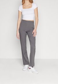 Biała krótka bluzka z krótkim rękawem w połączeniu z szarymi spodniami o dopasowanym kroju. Model nosi białe trampki z czerwonymi akcentami. Gładki materiał, dopasowany fason.