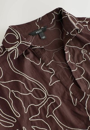 Camicia in lino marrone con ricamo floreale astratto bianco, caratterizzata da un colletto appuntito e un'etichetta che indica il marchio NEXT.