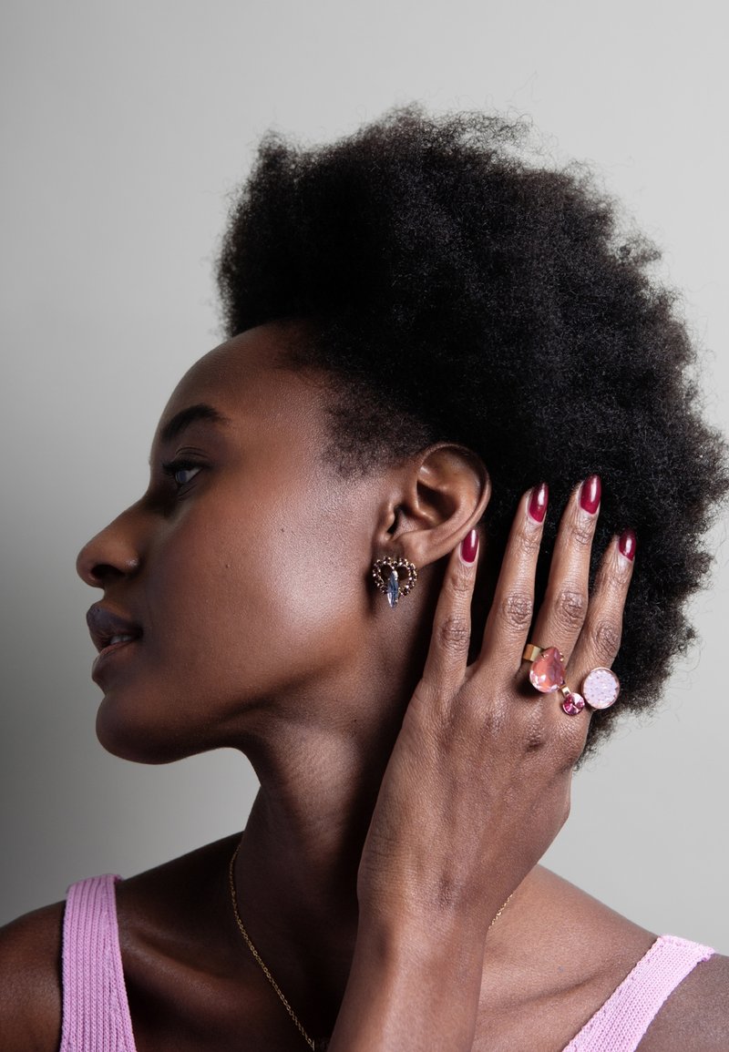 Gouden en gekleurde edelsteen oorbellen en ringen op een model. De oorbellen hebben een ingewikkeld ontwerp, terwijl de ringen verschillende vormen en stenen tonen.