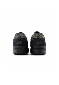 Ett par svarta New Balance-sneakers med fläckig hälkrage och logotyp synlig från baksidan på en vit bakgrund.